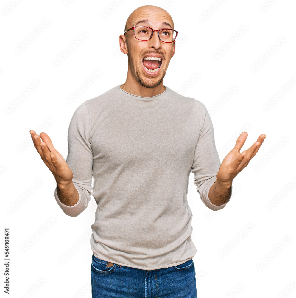 Bald man with beard wearing casual clothes and glasses crazy and mad shouting and yelling with aggressive expression and arms raised. frustration concept. Bald man with beard wearing casual clothes and glasses crazy and mad shouting and yelling with aggressive expression and arms raised. frustration concept.