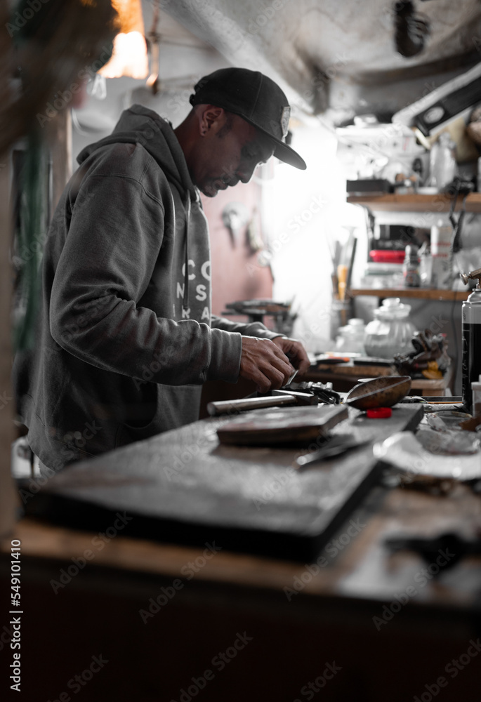 A craftsman jeweler is cutting a metal piece to create a jewel