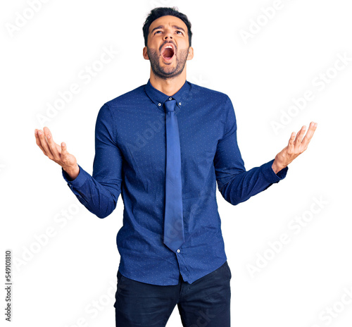 Young handsome hispanic man wearing business clothes crazy and mad shouting and yelling with aggressive expression and arms raised. frustration concept.