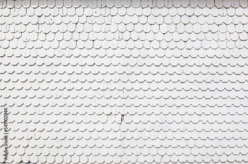Fassade verkleidet mit weiß gestrichenen Schindel aus Holz. Schindel auf Gebäude. Facade clad with white painted wooden shingles. White weathered shingles on building.