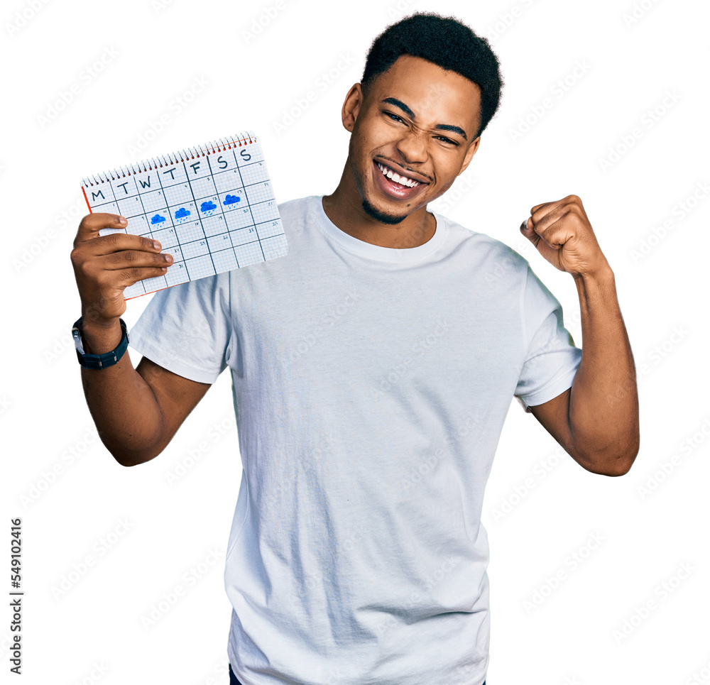 Young african american man holding rainy weather calendar screaming proud, celebrating victory and success very excited with raised arms Young african american man holding rainy weather calendar screaming proud, celebrating victory and success very excited with raised arms