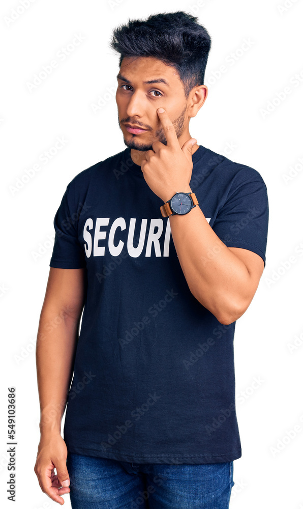 Handsome latin american young man wearing security t shirt pointing to the eye watching you gesture, suspicious expression Handsome latin american young man wearing security t shirt pointing to the eye watching you gesture, suspicious expression