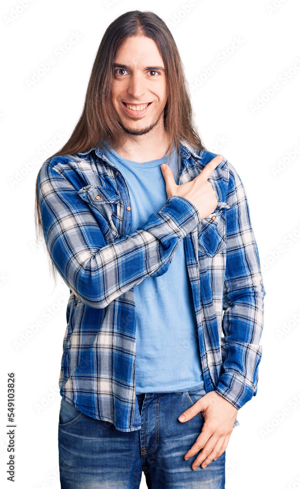 Young adult man with long hair wearing casual shirt cheerful with a smile of face pointing with hand and finger up to the side with happy and natural expression on face Young adult man with long hair wearing casual shirt cheerful with a smile of face pointing with hand and finger up to the side with happy and natural expression on face