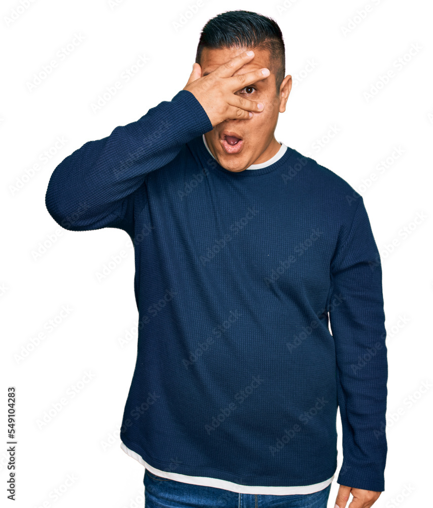 Young latin man wearing casual clothes peeking in shock covering face and eyes with hand, looking through fingers with embarrassed expression. Young latin man wearing casual clothes peeking in shock covering face and eyes with hand, looking through fingers with embarrassed expression.