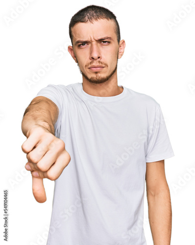 Hispanic young man wearing casual white t shirt looking unhappy and angry showing rejection and negative with thumbs down gesture. bad expression.