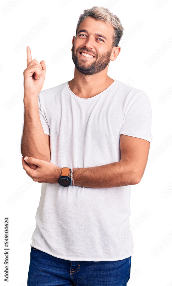 Young handsome blond man wearing casual t-shirt cheerful with a smile of face pointing with hand and finger up to the side with happy and natural expression on face Young handsome blond man wearing casual t-shirt cheerful with a smile of face pointing with hand and finger up to the side with happy and natural expression on face