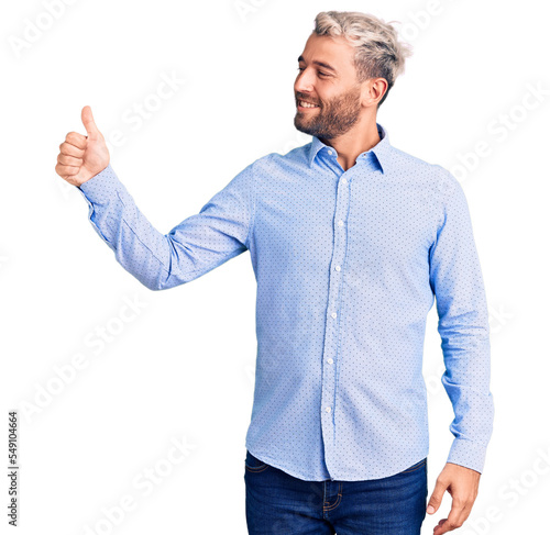 Young handsome blond man wearing elegant shirt looking proud, smiling doing thumbs up gesture to the side