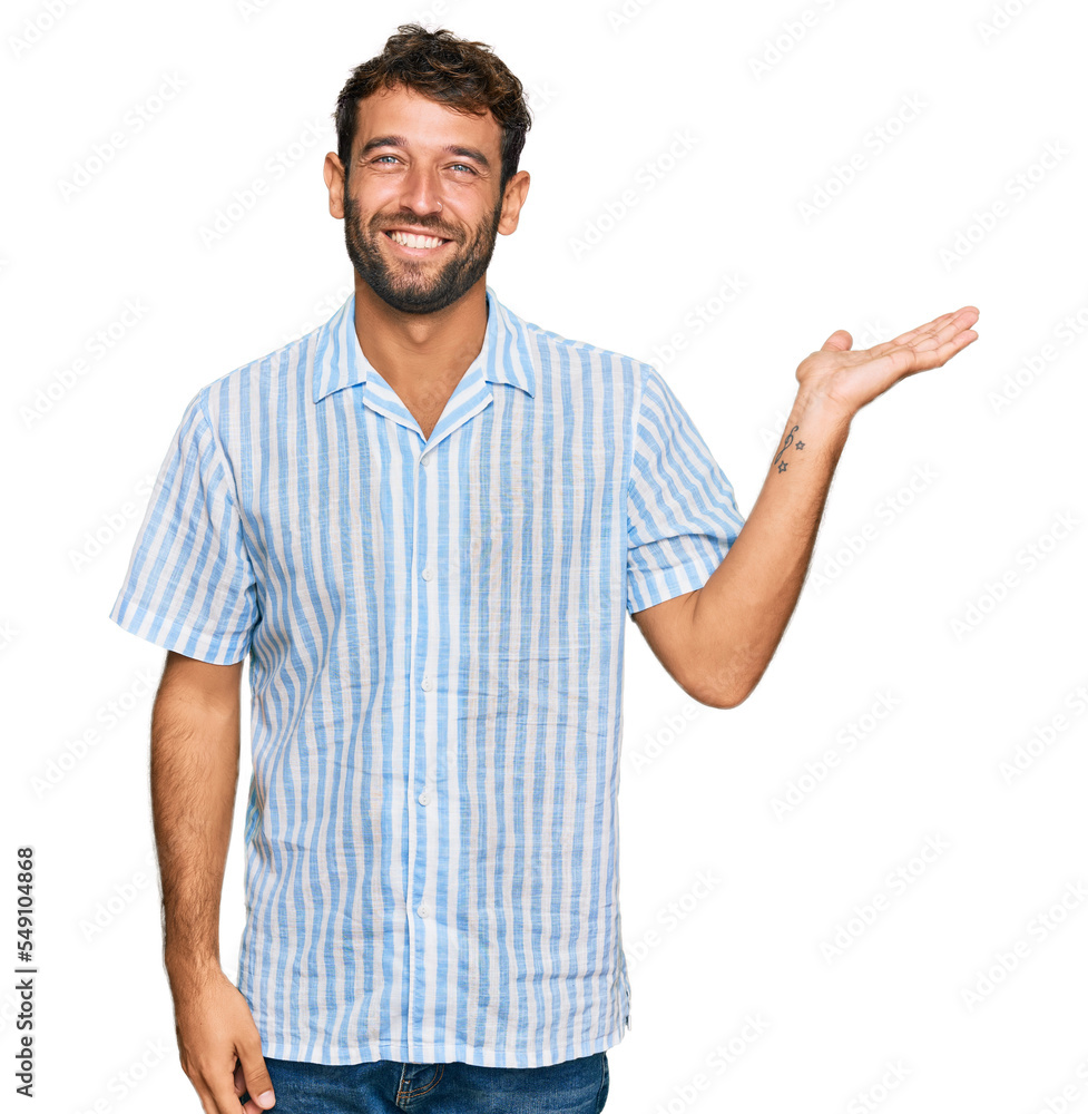Handsome young man with beard wearing casual fresh shirt smiling cheerful presenting and pointing with palm of hand looking at the camera. Handsome young man with beard wearing casual fresh shirt smiling cheerful presenting and pointing with palm of hand looking at the camera.