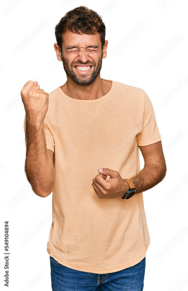 Handsome young man with beard wearing casual tshirt celebrating surprised and amazed for success with arms raised and eyes closed. winner concept. Handsome young man with beard wearing casual tshirt celebrating surprised and amazed for success with arms raised and eyes closed. winner concept.
