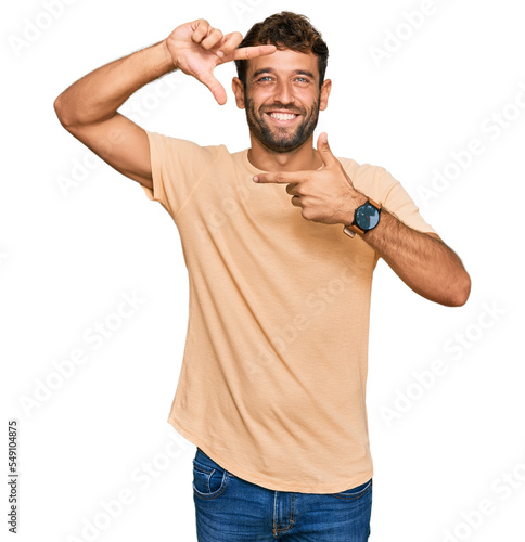 Handsome young man with beard wearing casual tshirt smiling making frame with hands and fingers with happy face. creativity and photography concept.