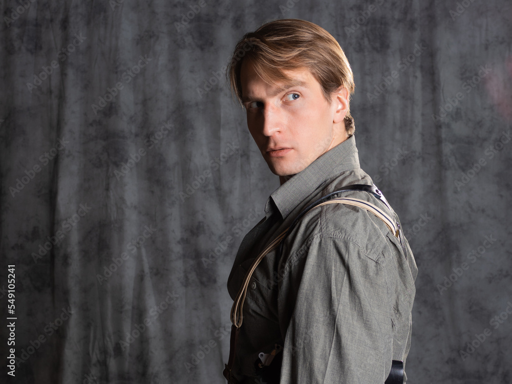 A lawyer with a pistol in a holster, gray shirt and trousers with suspenders, retro style. A young man poses in the studio on a gray background A lawyer with a pistol in a holster, gray shirt and trousers with suspenders, retro style. A young man poses in the studio on a gray background