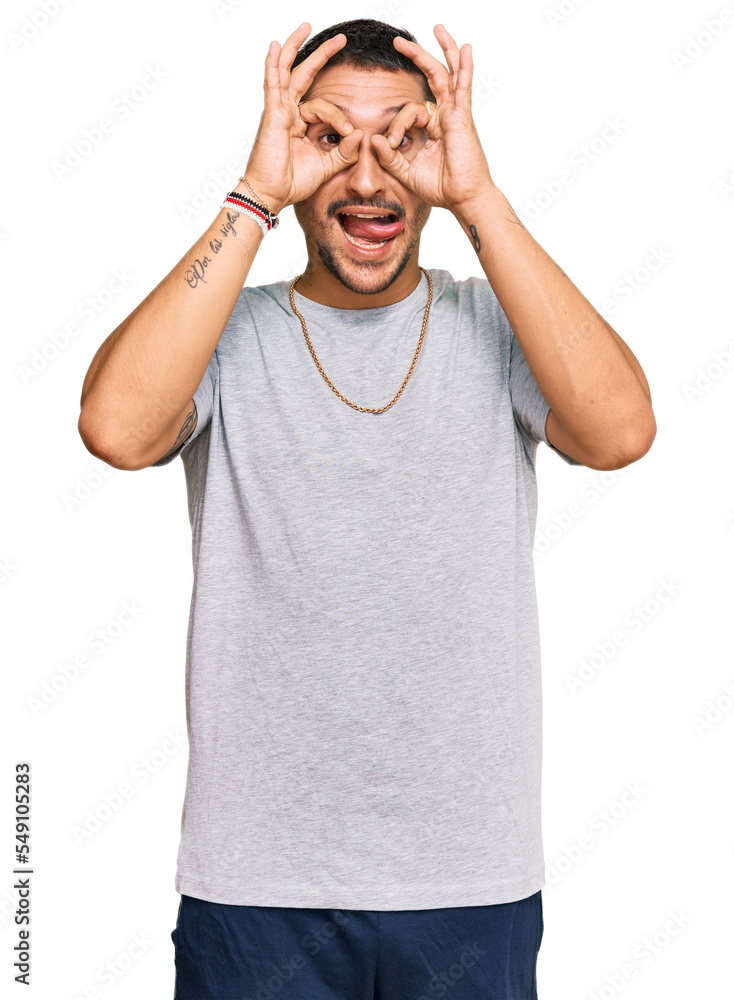 Handsome man with tattoos wearing 90s style doing ok gesture like binoculars sticking tongue out, eyes looking through fingers. crazy expression. Handsome man with tattoos wearing 90s style doing ok gesture like binoculars sticking tongue out, eyes looking through fingers. crazy expression.