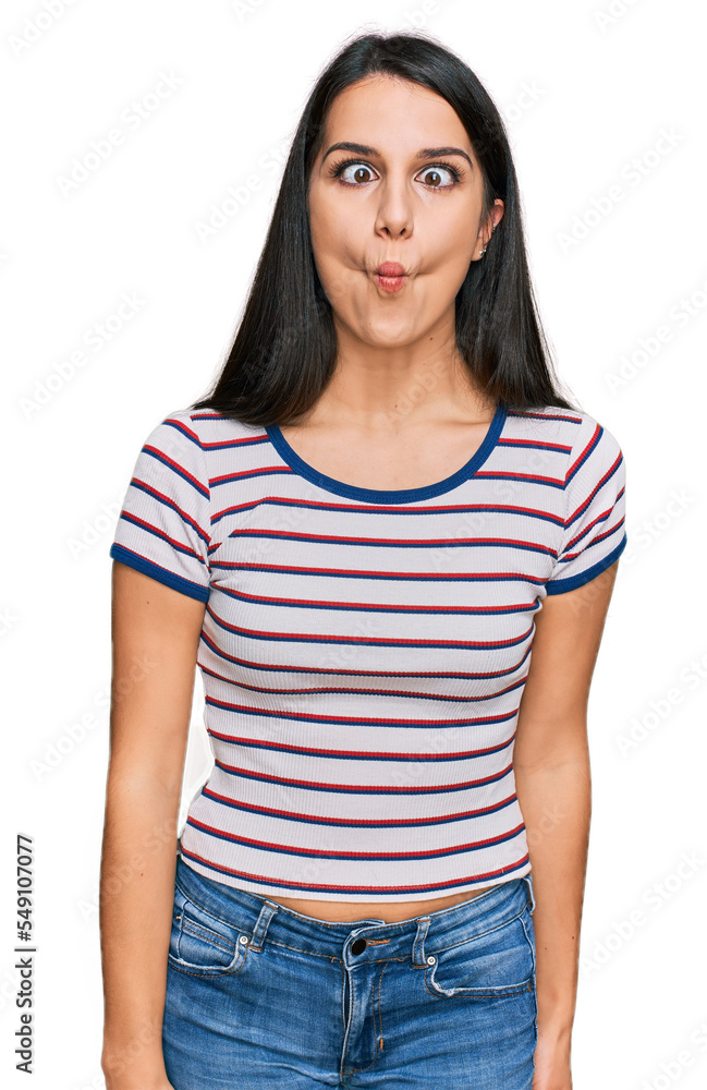 Fototapeta premium Young hispanic girl wearing casual striped t shirt making fish face with lips, crazy and comical gesture. funny expression.