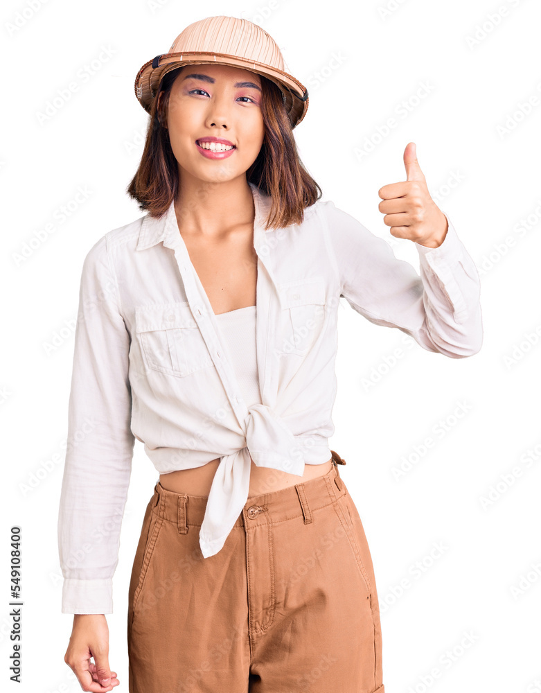 Young beautiful chinese girl wearing explorer hat smiling happy and positive, thumb up doing excellent and approval sign Young beautiful chinese girl wearing explorer hat smiling happy and positive, thumb up doing excellent and approval sign