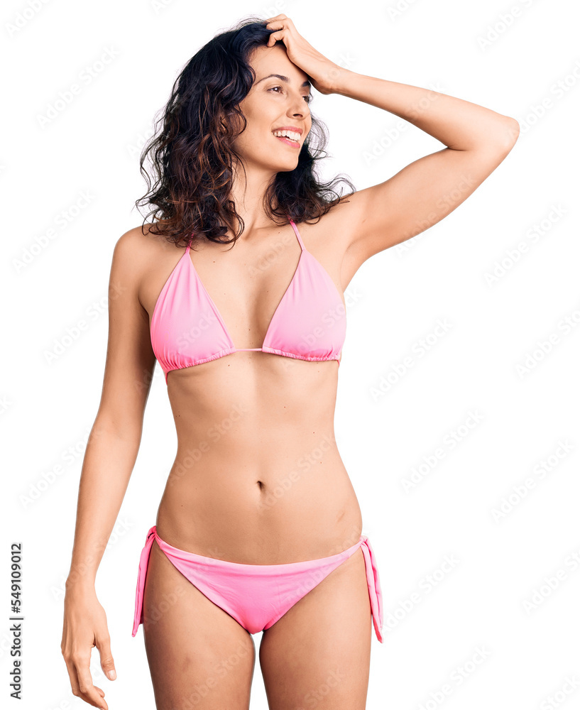 Young beautiful hispanic woman wearing bikini smiling confident touching hair with hand up gesture, posing attractive and fashionable Young beautiful hispanic woman wearing bikini smiling confident touching hair with hand up gesture, posing attractive and fashionable