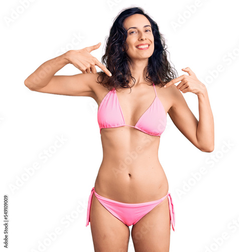Young beautiful hispanic woman wearing bikini looking confident with smile on face, pointing oneself with fingers proud and happy. © Krakenimages.com