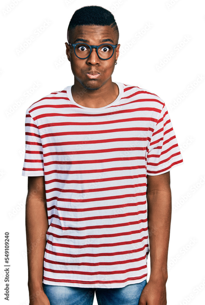 Young african american man wearing casual t shirt and glasses puffing cheeks with funny face. mouth inflated with air, crazy expression. Young african american man wearing casual t shirt and glasses puffing cheeks with funny face. mouth inflated with air, crazy expression.