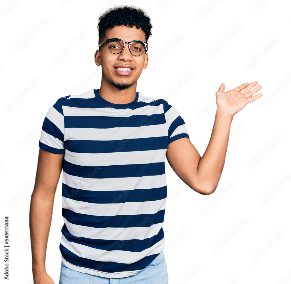 Young african american man wearing casual clothes and glasses smiling cheerful presenting and pointing with palm of hand looking at the camera. Young african american man wearing casual clothes and glasses smiling cheerful presenting and pointing with palm of hand looking at the camera.