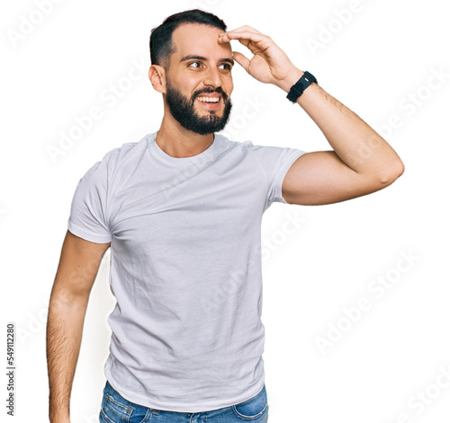 Young man with beard wearing casual white t shirt smiling confident touching hair with hand up gesture, posing attractive and fashionable © Krakenimages.com