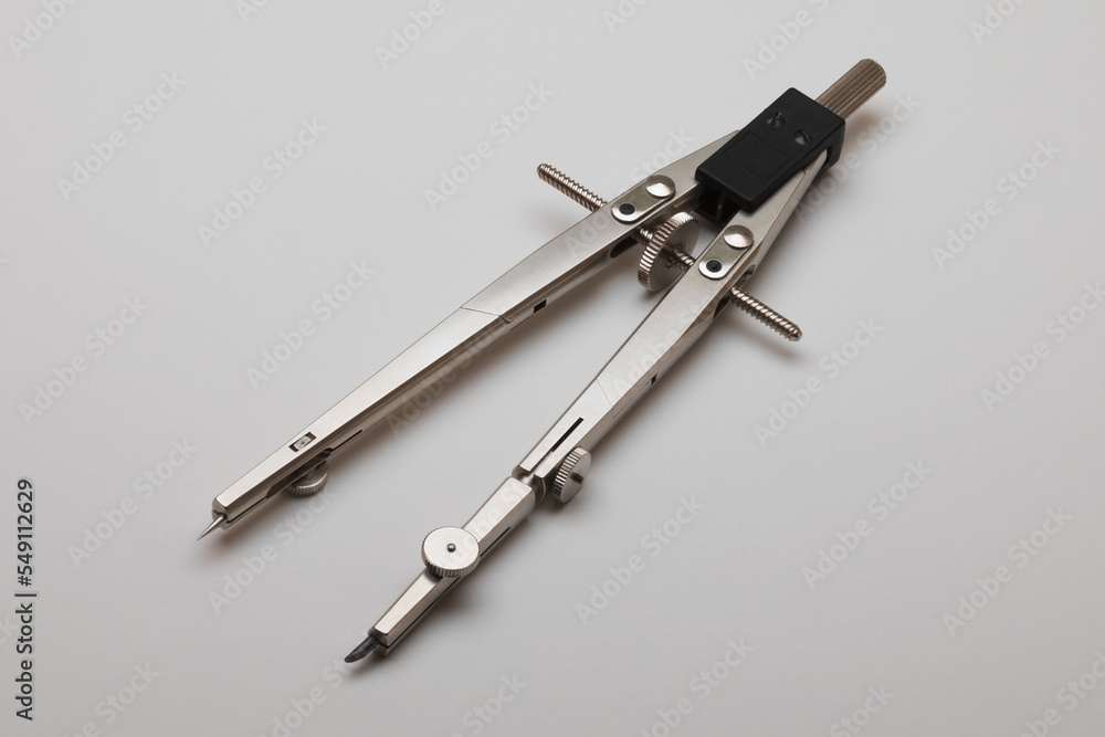 Pair of drawing compasses lying on a plain light background Pair of drawing compasses lying on a plain light background