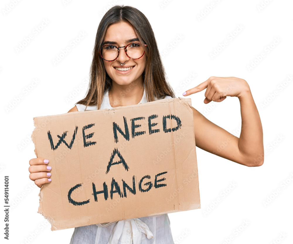 Young hispanic woman holding we need a change banner pointing finger to one self smiling happy and proud Young hispanic woman holding we need a change banner pointing finger to one self smiling happy and proud