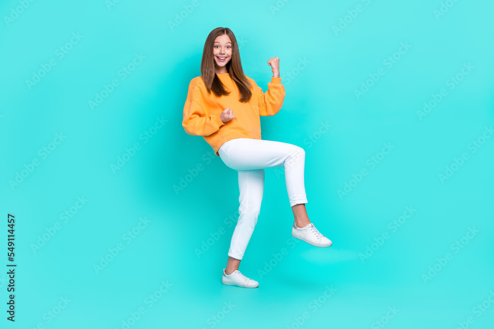 Full length photo of excited funny childish schoolgirl teenager celebrating her win competition fists up isolated on cyan color background Full length photo of excited funny childish schoolgirl teenager celebrating her win competition fists up isolated on cyan color background