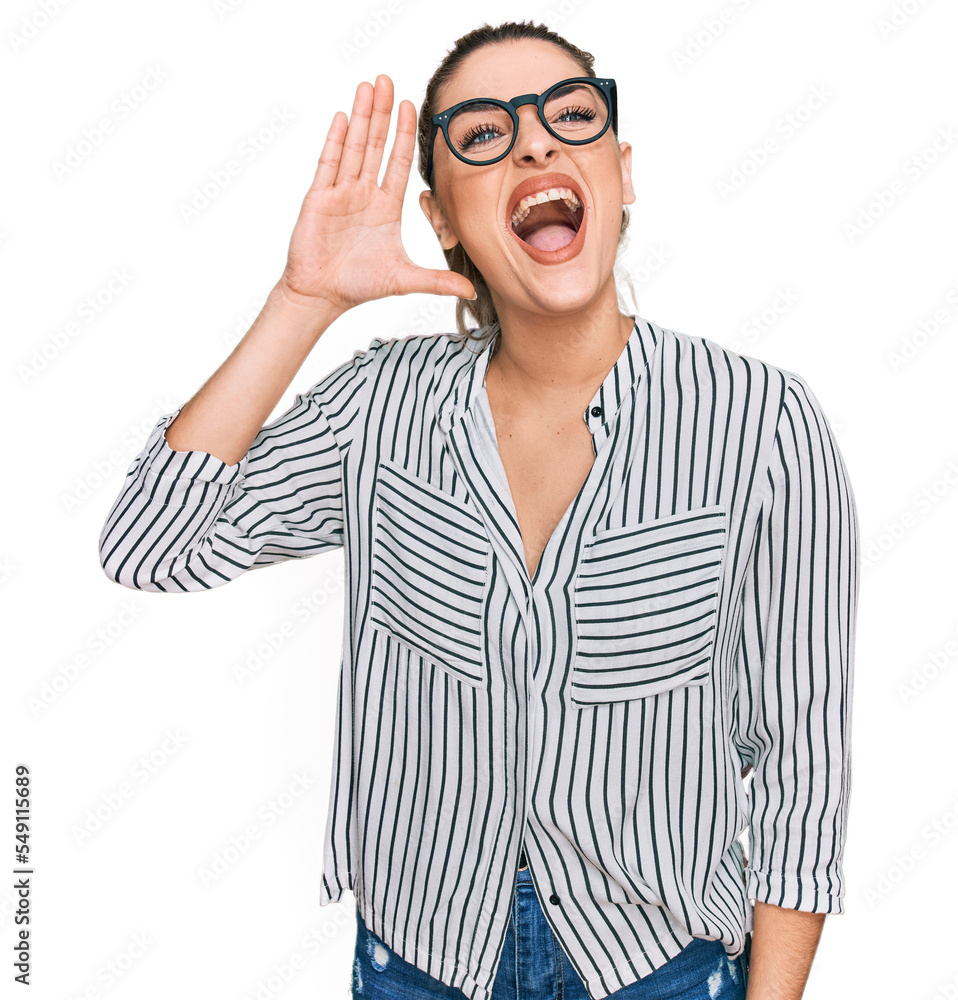 Young caucasian woman wearing business shirt and glasses shouting and screaming loud to side with hand on mouth. communication concept. Young caucasian woman wearing business shirt and glasses shouting and screaming loud to side with hand on mouth. communication concept.