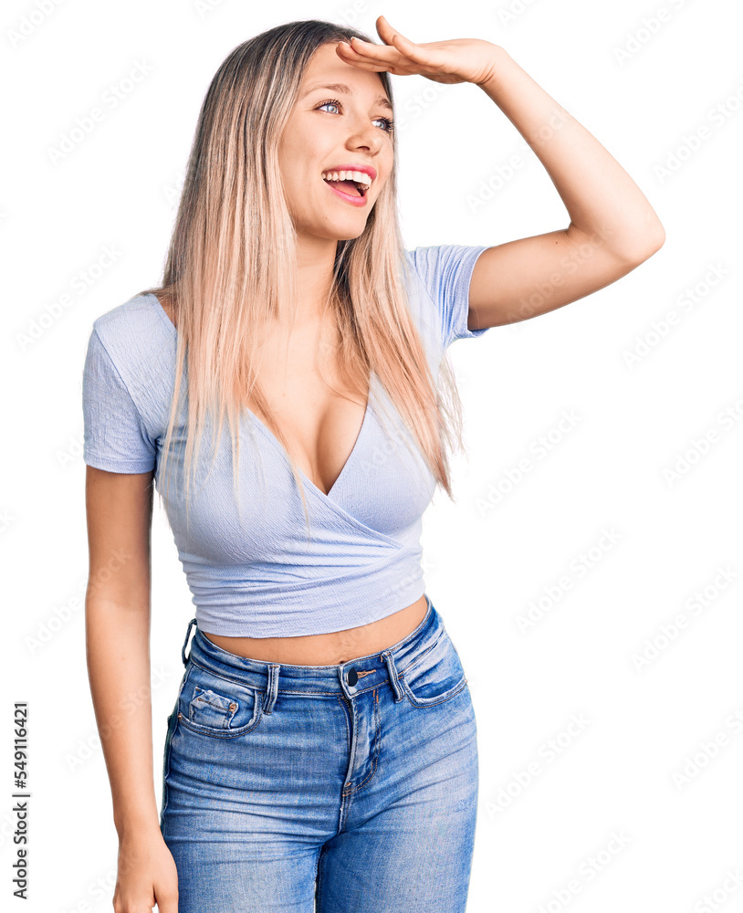 Young beautiful blonde woman wearing casual clothes very happy and smiling looking far away with hand over head. searching concept. Young beautiful blonde woman wearing casual clothes very happy and smiling looking far away with hand over head. searching concept.