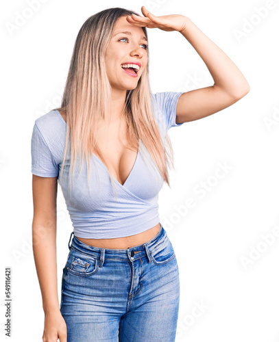 Young beautiful blonde woman wearing casual clothes very happy and smiling looking far away with hand over head. searching concept.