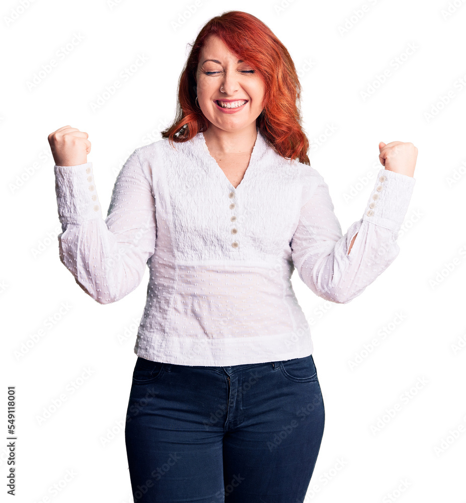 Young beautiful redhead woman wearing casual shirt very happy and excited doing winner gesture with arms raised, smiling and screaming for success. celebration concept. Young beautiful redhead woman wearing casual shirt very happy and excited doing winner gesture with arms raised, smiling and screaming for success. celebration concept.