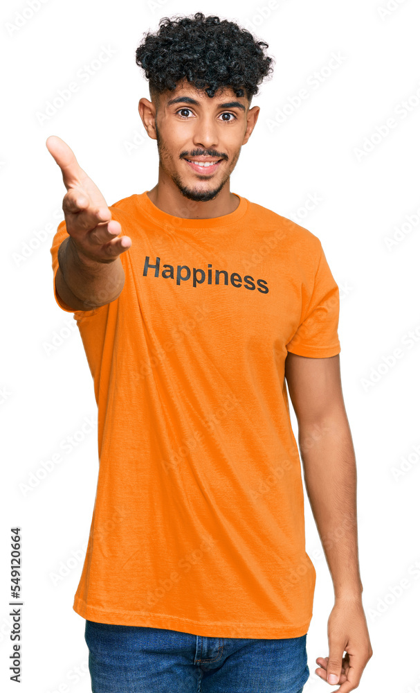 Young arab man wearing tshirt with happiness word message smiling friendly offering handshake as greeting and welcoming. successful business. Young arab man wearing tshirt with happiness word message smiling friendly offering handshake as greeting and welcoming. successful business.