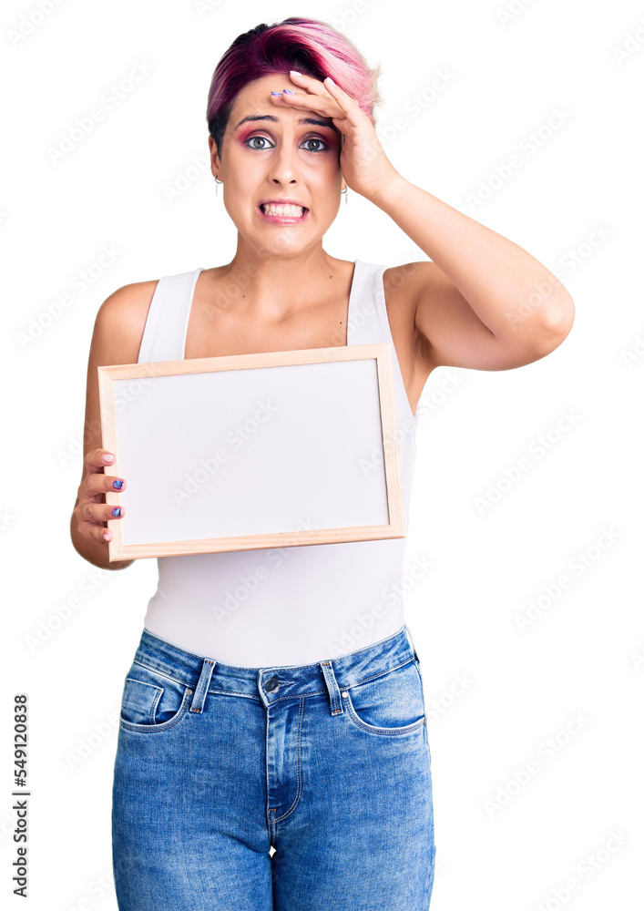 Young beautiful woman with pink hair holding empty white chalkboard stressed and frustrated with hand on head, surprised and angry face Young beautiful woman with pink hair holding empty white chalkboard stressed and frustrated with hand on head, surprised and angry face