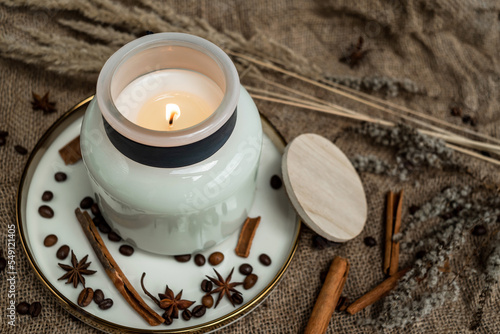 Aesthetic composition of candles, anise, cinnamon sticks and coffee beans on a background of burlap, decorated with dried flowers