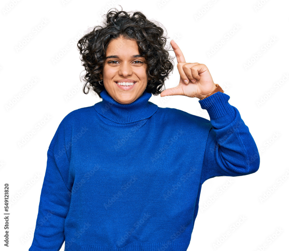 Young hispanic woman with curly hair wearing turtleneck sweater smiling and confident gesturing with hand doing small size sign with fingers looking and the camera. measure concept. Young hispanic woman with curly hair wearing turtleneck sweater smiling and confident gesturing with hand doing small size sign with fingers looking and the camera. measure concept.