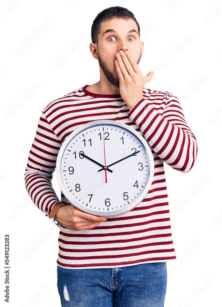 Young handsome man holding big clock covering mouth with hand, shocked and afraid for mistake. surprised expression Young handsome man holding big clock covering mouth with hand, shocked and afraid for mistake. surprised expression