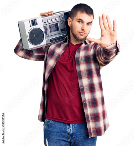 Young handsome man listening to music holding boombox with open hand doing stop sign with serious and confident expression, defense gesture