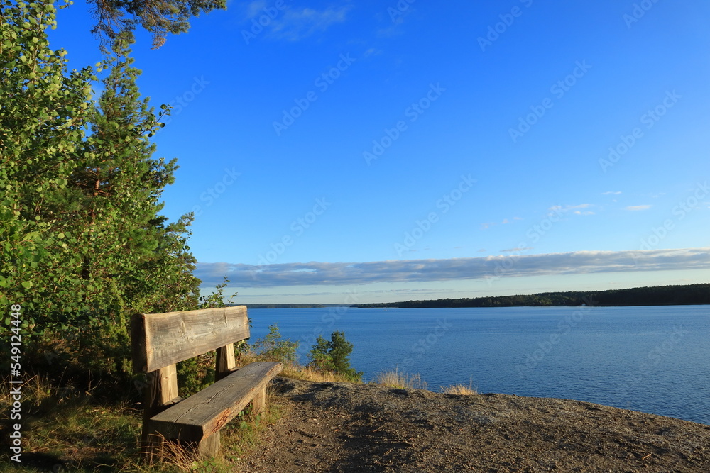 Romantic view over the Swedish lake called Malaren or Mälaren. Old wooden bench for relaxation. Blue sky and green nature. Copy space for text. Järfälla, Stockholm, Sweden, Scandinavia, Europe, 2021.
