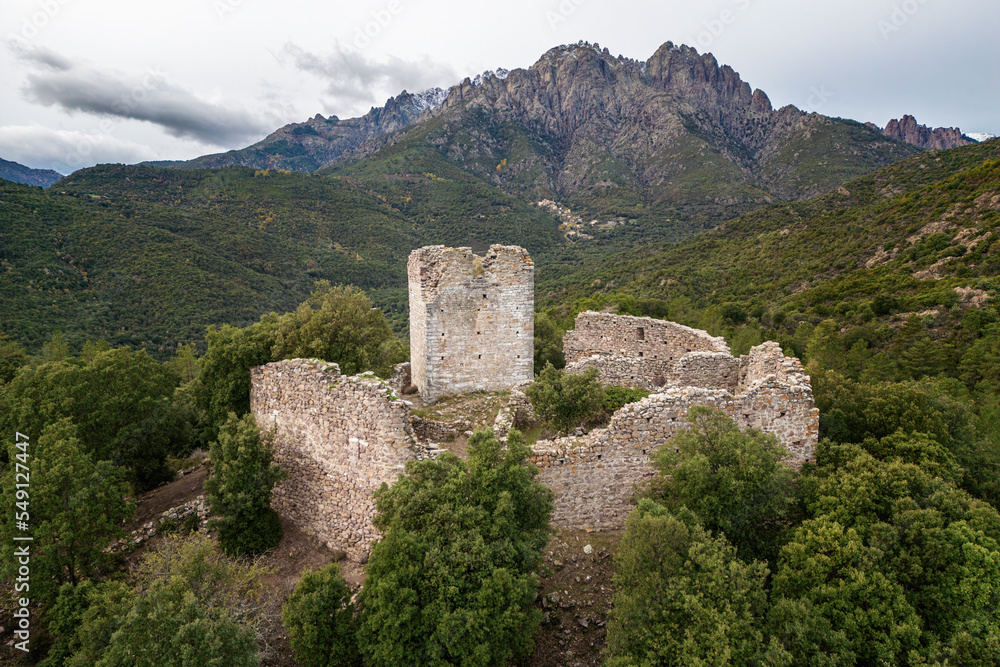 Aerial view of the ruins of Castellu di Seravalle in Corsica, a military fortress built in the 11th century on a hilltop with the village of Popolasca iwith les Aiguilles de Popolasca in the distance Aerial view of the ruins of Castellu di Seravalle in Corsica, a military fortress built in the 11th century on a hilltop with the village of Popolasca iwith les Aiguilles de Popolasca in the distance