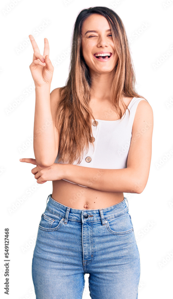 Young beautiful girl wearing casual sleeveless t shirt smiling with happy face winking at the camera doing victory sign. number two. Young beautiful girl wearing casual sleeveless t shirt smiling with happy face winking at the camera doing victory sign. number two.