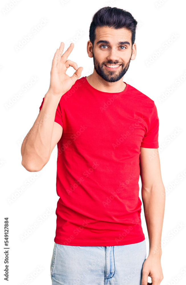 Young handsome man with beard wearing casual t-shirt smiling positive doing ok sign with hand and fingers. successful expression. Young handsome man with beard wearing casual t-shirt smiling positive doing ok sign with hand and fingers. successful expression.
