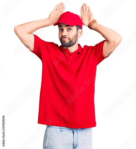 Young handsome man with beard wearing delivery uniform doing bunny ears gesture with hands palms looking cynical and skeptical. easter rabbit concept.