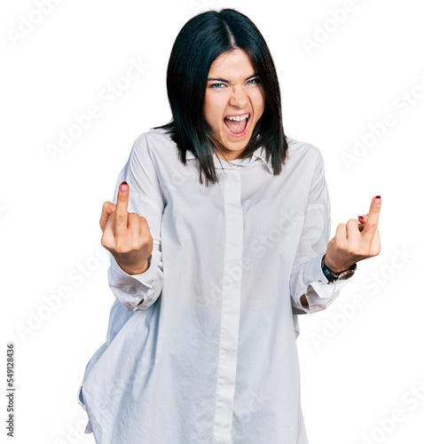 Young brunette woman with blue eyes wearing oversize white shirt showing middle finger doing fuck you bad expression, provocation and rude attitude. screaming excited