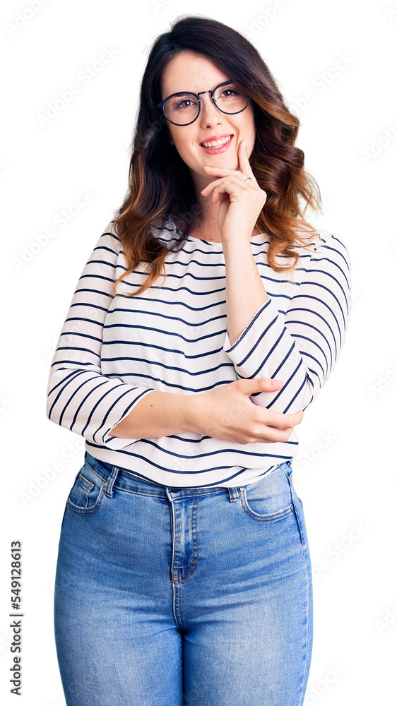 Beautiful young brunette woman wearing casual clothes and glasses looking confident at the camera with smile with crossed arms and hand raised on chin. thinking positive. Beautiful young brunette woman wearing casual clothes and glasses looking confident at the camera with smile with crossed arms and hand raised on chin. thinking positive.