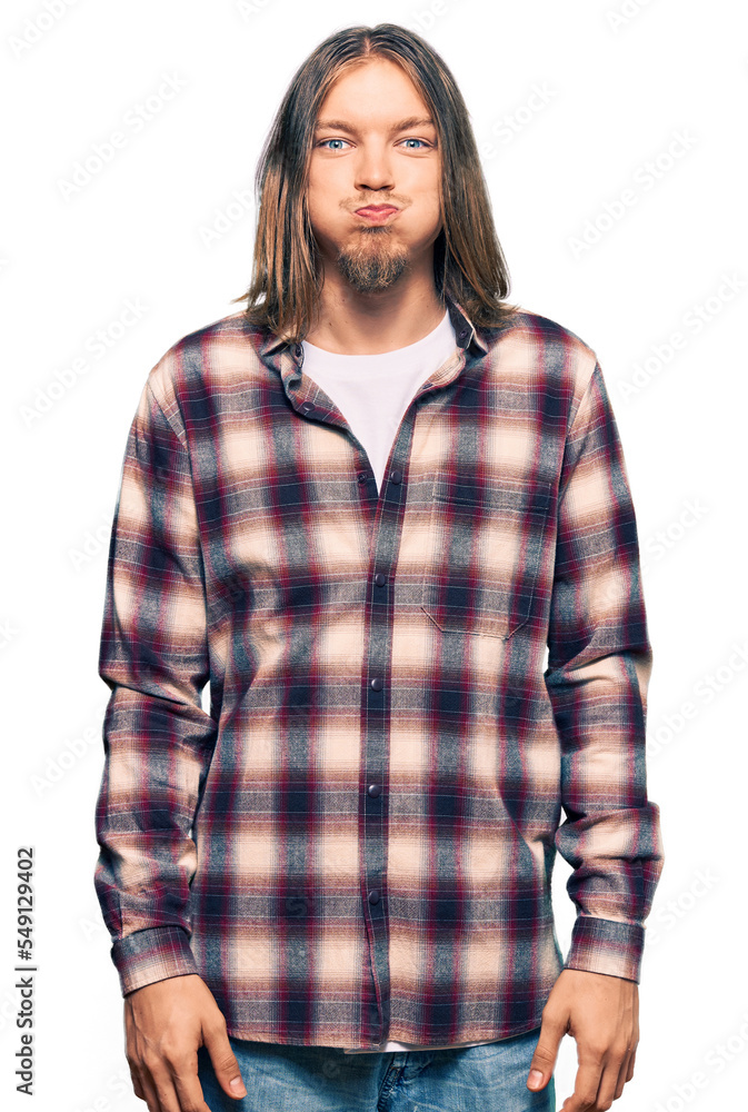 Handsome caucasian man with long hair wearing hipster shirt puffing cheeks with funny face. mouth inflated with air, crazy expression. Handsome caucasian man with long hair wearing hipster shirt puffing cheeks with funny face. mouth inflated with air, crazy expression.
