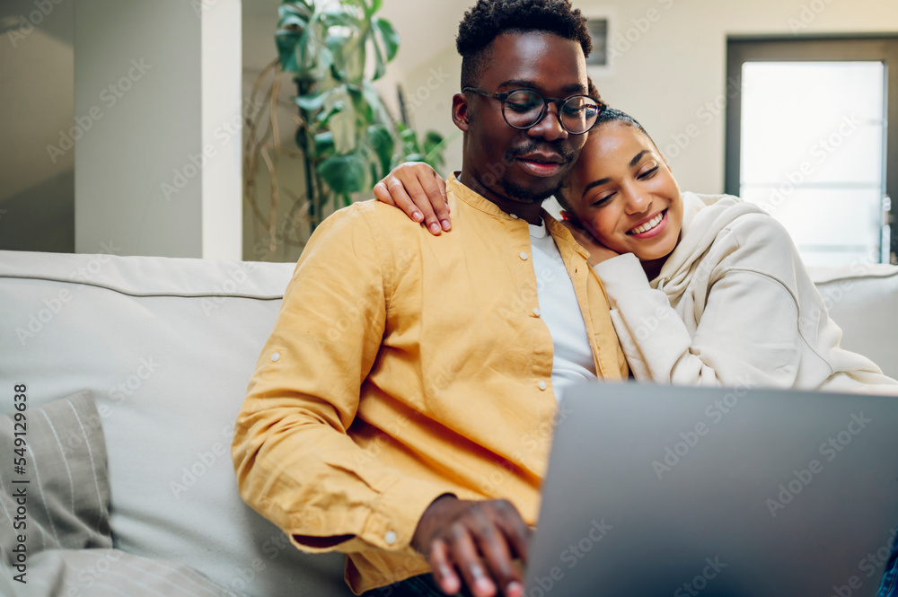 Multiracial couple using laptop while sitting on a sofa at home Multiracial couple using laptop while sitting on a sofa at home