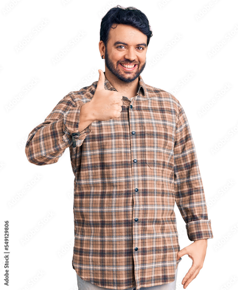 Young hispanic man wearing casual clothes doing happy thumbs up gesture with hand. approving expression looking at the camera showing success. Young hispanic man wearing casual clothes doing happy thumbs up gesture with hand. approving expression looking at the camera showing success.