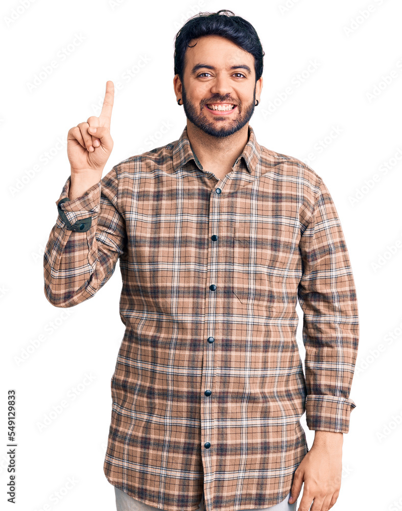 Young hispanic man wearing casual clothes showing and pointing up with finger number one while smiling confident and happy. Young hispanic man wearing casual clothes showing and pointing up with finger number one while smiling confident and happy.