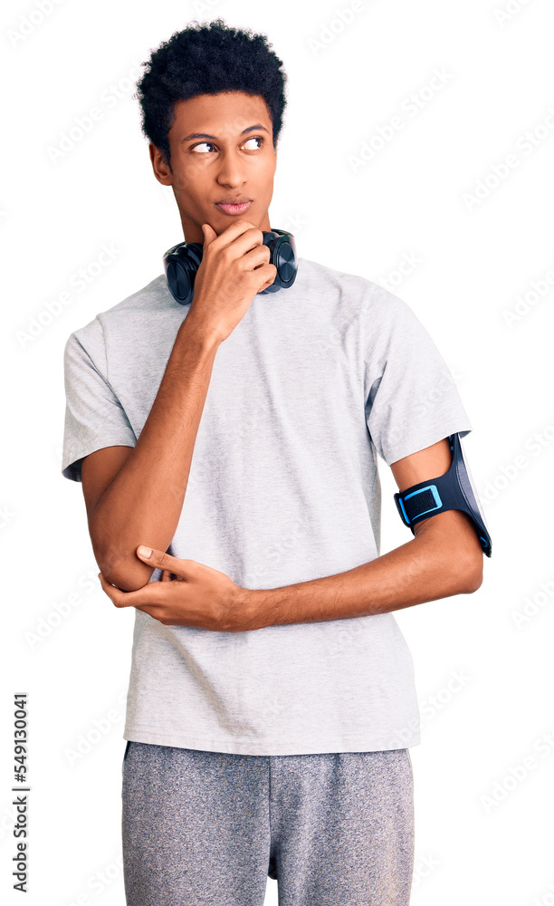 Young african american man wearing gym clothes and using headphones serious face thinking about question with hand on chin, thoughtful about confusing idea Young african american man wearing gym clothes and using headphones serious face thinking about question with hand on chin, thoughtful about confusing idea