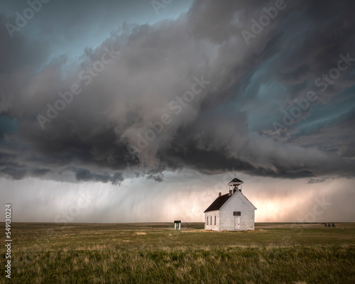 Severe thunderstorm over a rural church in the countryside. The church is in an open field with short grass.  A tornado looks like it might touchdown. 