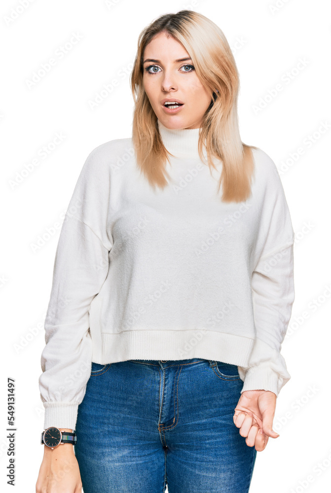 Young caucasian woman wearing casual winter sweater in shock face, looking skeptical and sarcastic, surprised with open mouth Young caucasian woman wearing casual winter sweater in shock face, looking skeptical and sarcastic, surprised with open mouth